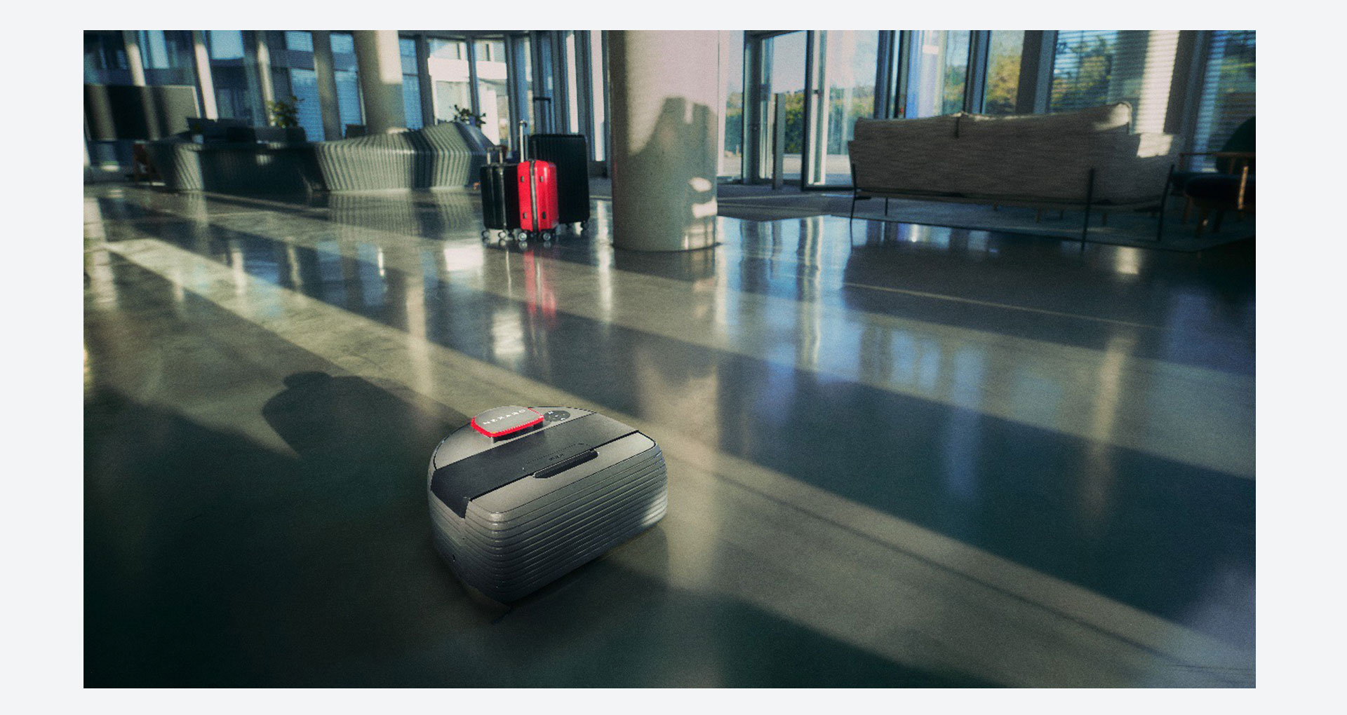Autonomer Reinigungsroboter von Nexaro fährt durch eine helle Hotellobby mit glänzendem Boden und Koffern im Hintergrund.