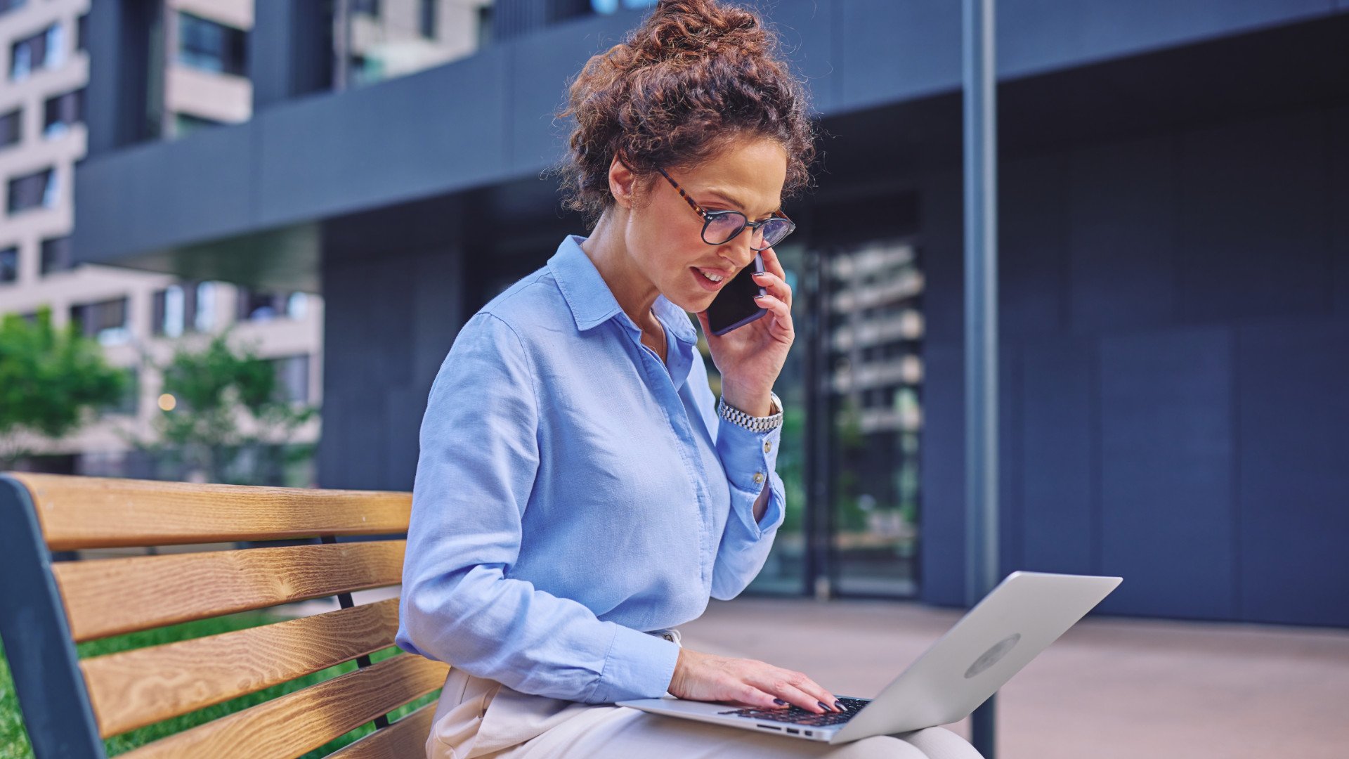 Eine Geschäftsfrau nutzt ihr privates Handy und Notebook für die Arbeit auf einer Parkbank