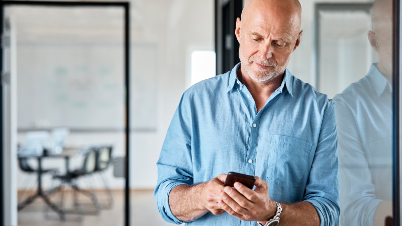 Ein älterer Mitarbeiter nutzt sein Smartphone im Büro