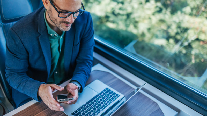 Geschäftsmann in der Bahn mit Handy und Laptop