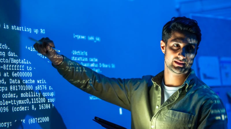 Ein IT-Experte deutet auf Code, der an eine Wand projiziert wird.