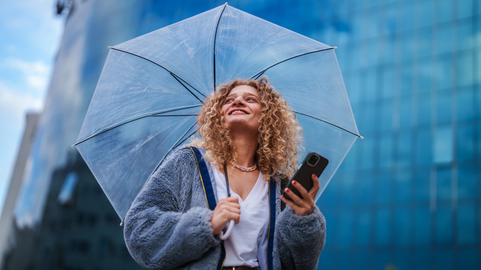 Eine Frau mit Regenschirm nutzt ein Smartphone.