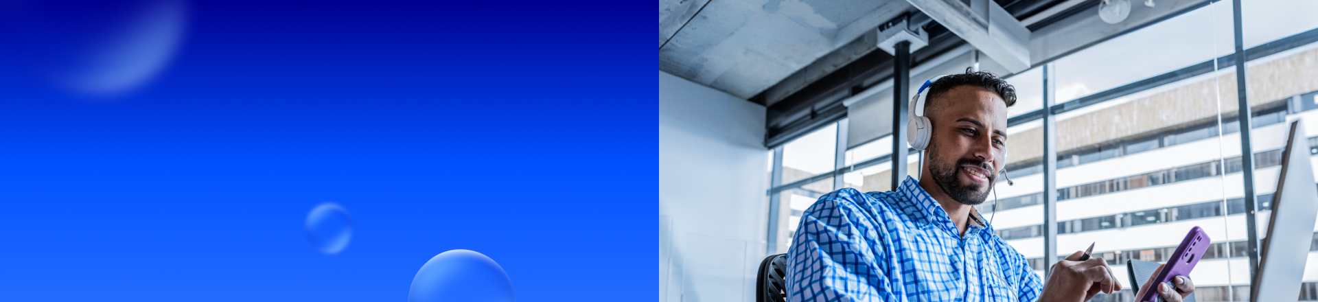 Abbildung: Mann mit Headset sitzt vor einem Computer Monitor und hält ein Smartphone in der Hand