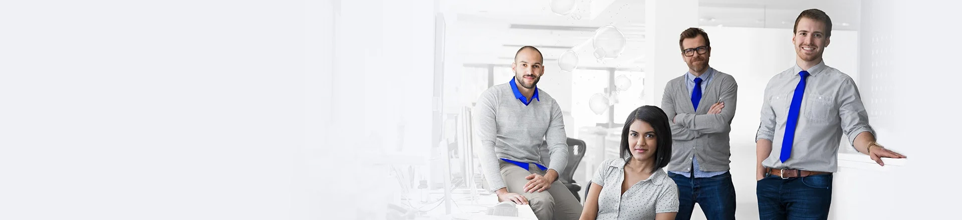 Vier Personen stehen und sitzen gemeinsam in einem Büro und posieren vor einem hellen Hintergrund.