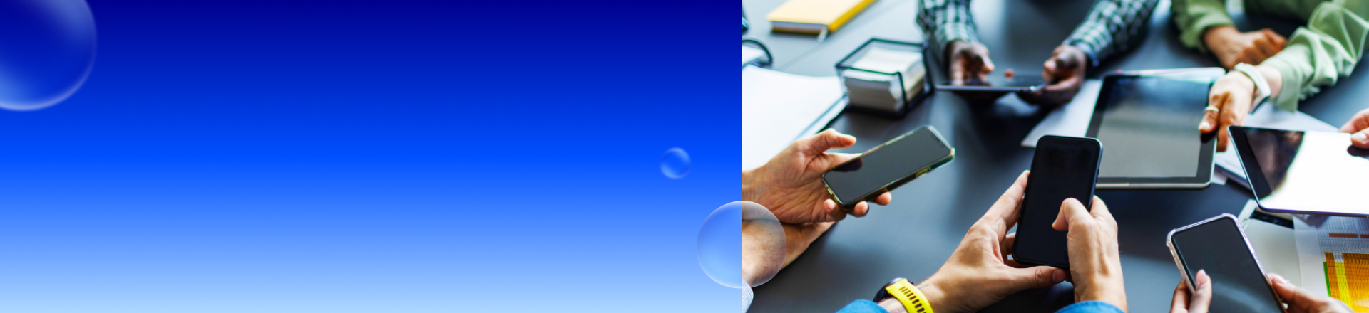 Mehrere Personen sitzen an einem Tisch und halten Smartphones und Tablets in den Händen, während Unterlagen und ein Notizbuch auf dem Tisch liegen.